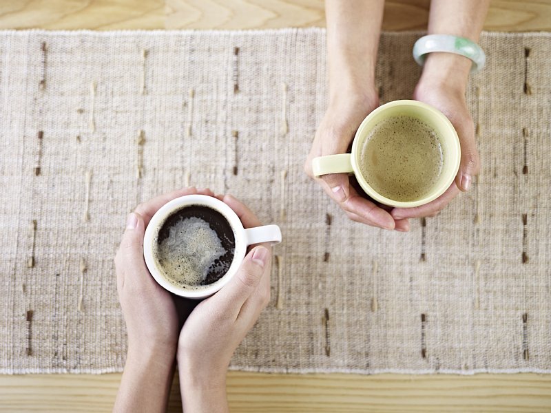 手に持ったカップに入ったコーヒーと手に持ったカップに入った緑茶