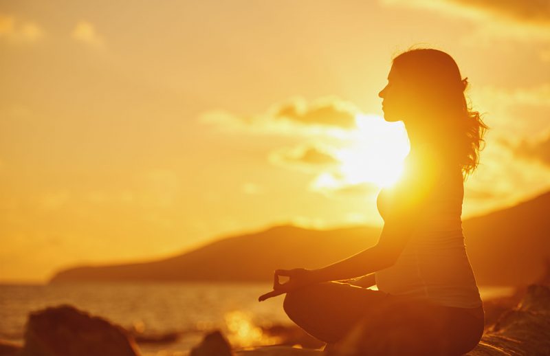 夕方に海辺で女性が瞑想をしている