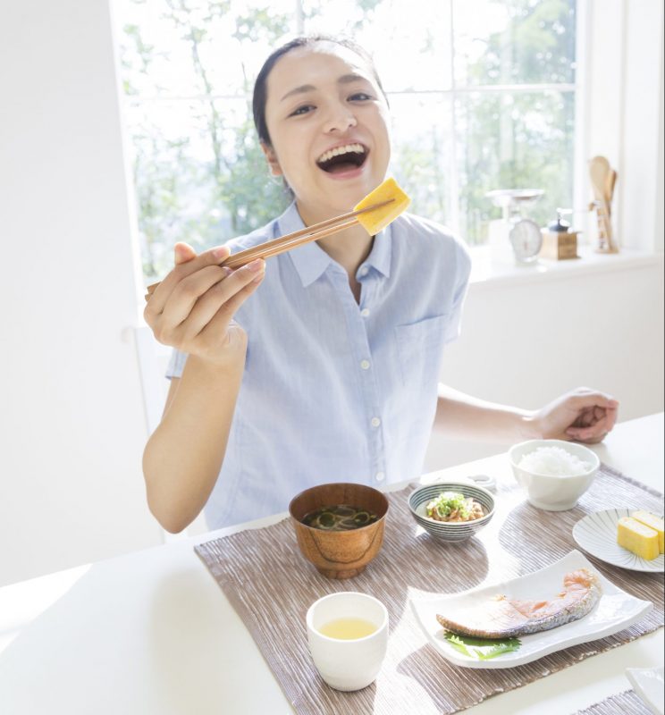 女性が朝食を食べているところ。卵焼きを手に笑顔