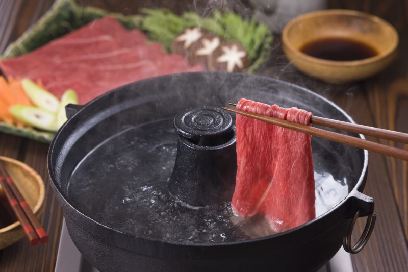 牛肉を箸で持ち、しゃぶしゃぶ用の鍋に入れている