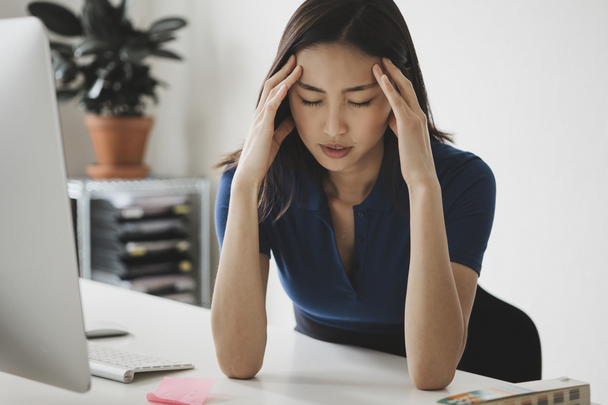 女性が青白い顔でデスクに向かってこめかみを押さえている