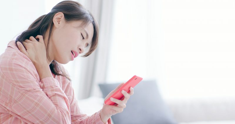 スマートフォンを手に首を押さえて苦しそうな女性