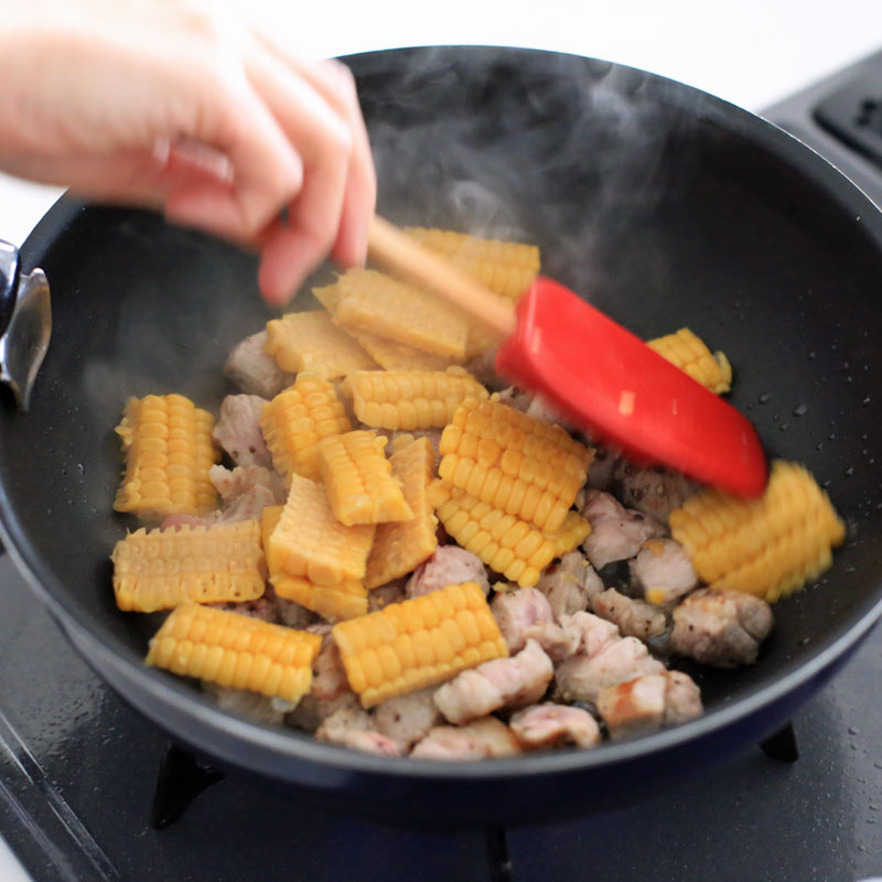 フライパンで豚肉ととうもろこしを炒めている