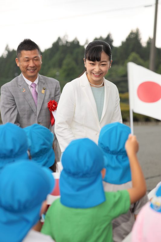 2019年7月24日に、アイスブルーのワンピースに白いジャケットをお召しになり馬術競技大会に出席された佳子さま。出迎えた園児に笑顔でお応えする。