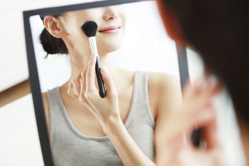 鏡の前でメイクブラシでメイクしている女性