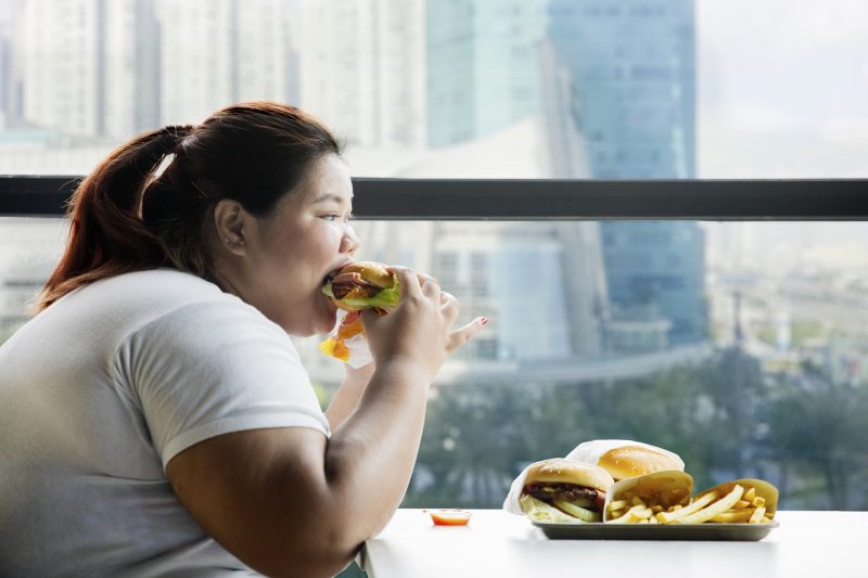 太った女性がハンバーガーにかぶりついている