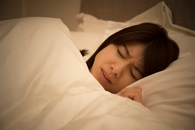 寝苦しそうに布団の中で眠る女性