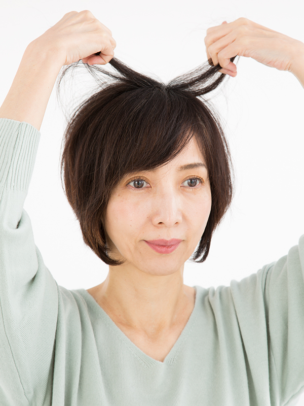 両手でハチ上の髪を持ち上げている女性