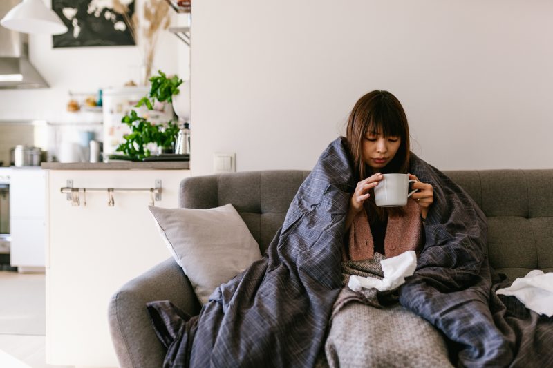 布団をかぶってスープを飲んでいる風邪を引いた女性