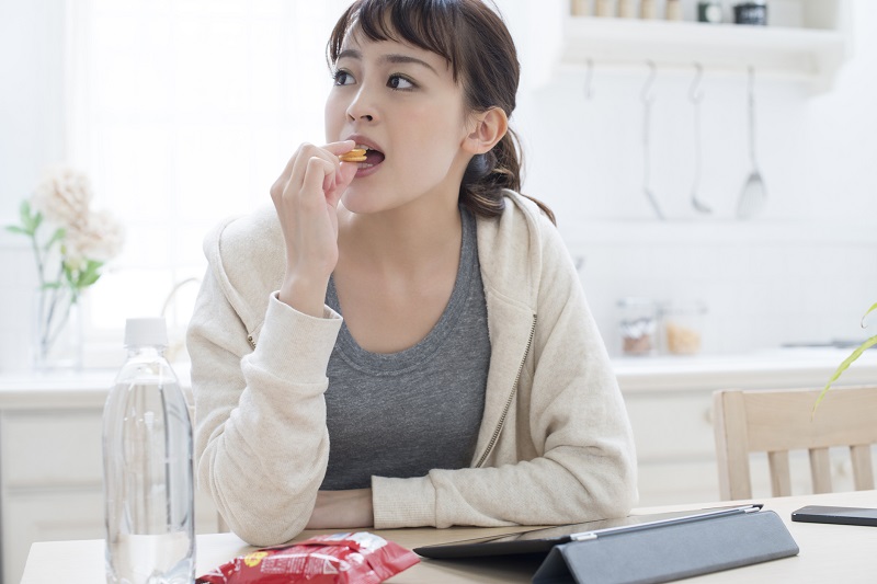 食卓でパソコンを開きながらお菓子を食べる女性の写真