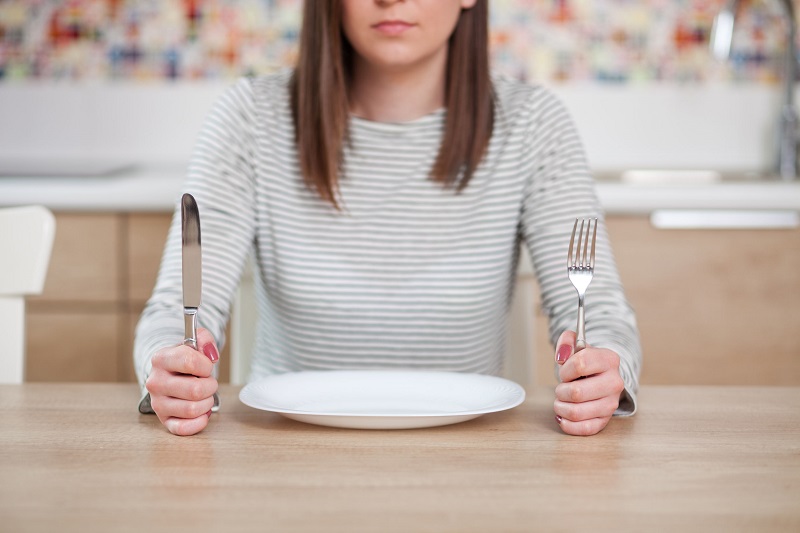 食卓の空のお皿とフォークとナイフを持った女性の画像