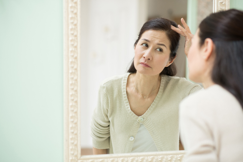 鏡を見ながら分け目を気にする中年女性の写真