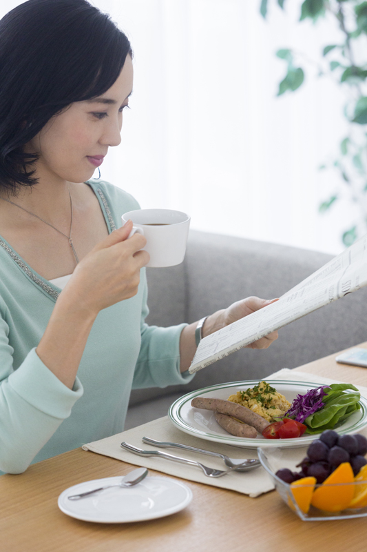 コーヒーを手にゆっくり朝食をとる女性