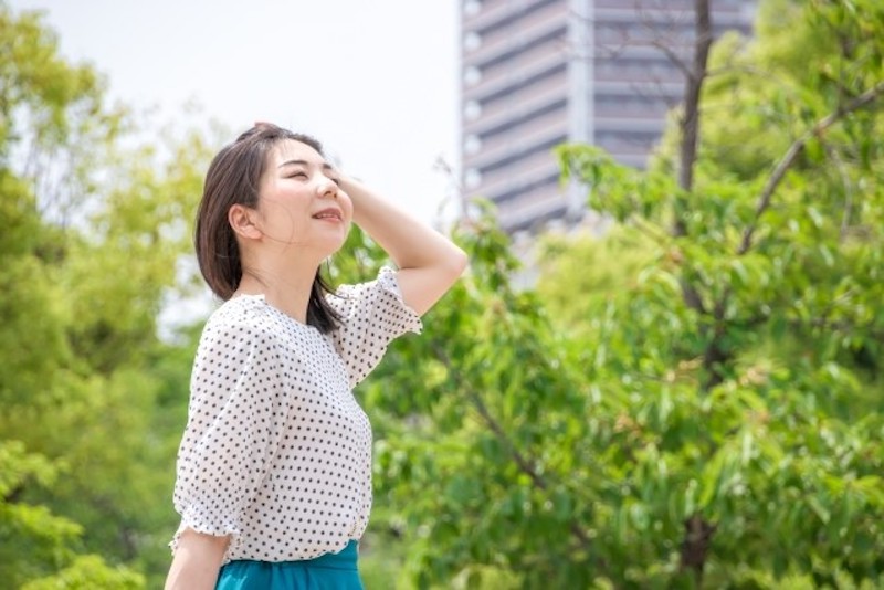 さわやかな雰囲気の木々の前に立つ女性