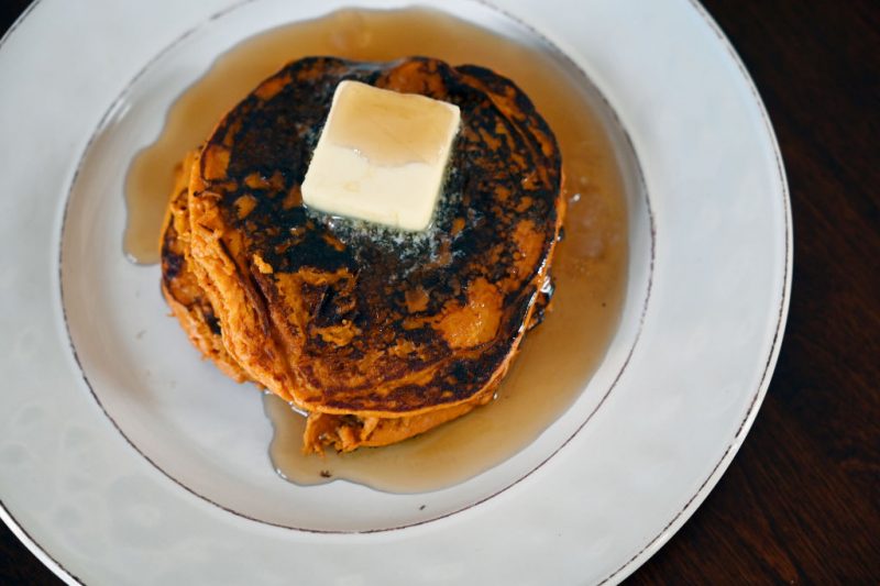 白い皿の上にのった焦げ目のついたホットケーキ上にバターがのって、メープルシロップがたっぷりかけられている