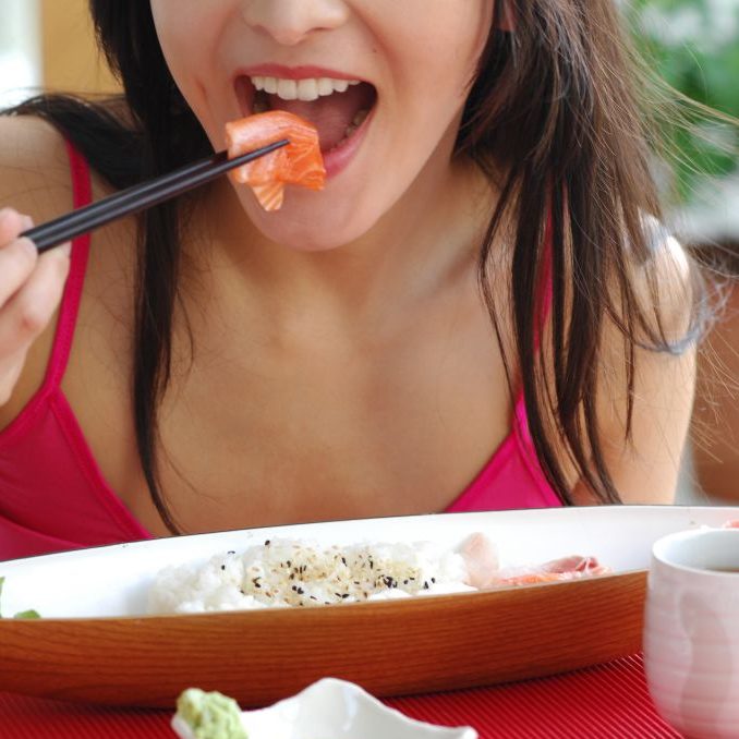 赤い服を着た女性が魚を食べている口元