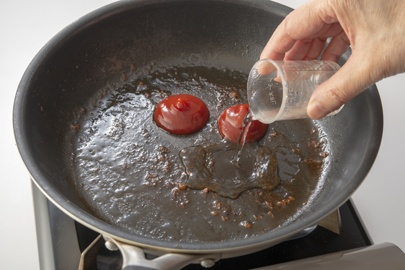 肉を焼いた後のフライパンに調味料を入れてソースを作っている