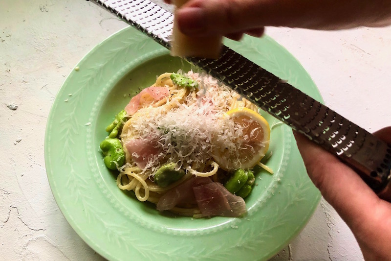 生ハムパスタがのった皿にゼスターグレーターで削ったチーズを削りかけている