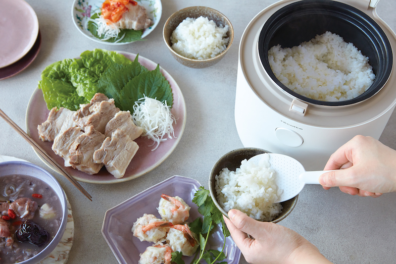 糖質オフ炊飯器からご飯をよそっているところ。周りにはゆで豚などの料理が並ぶ