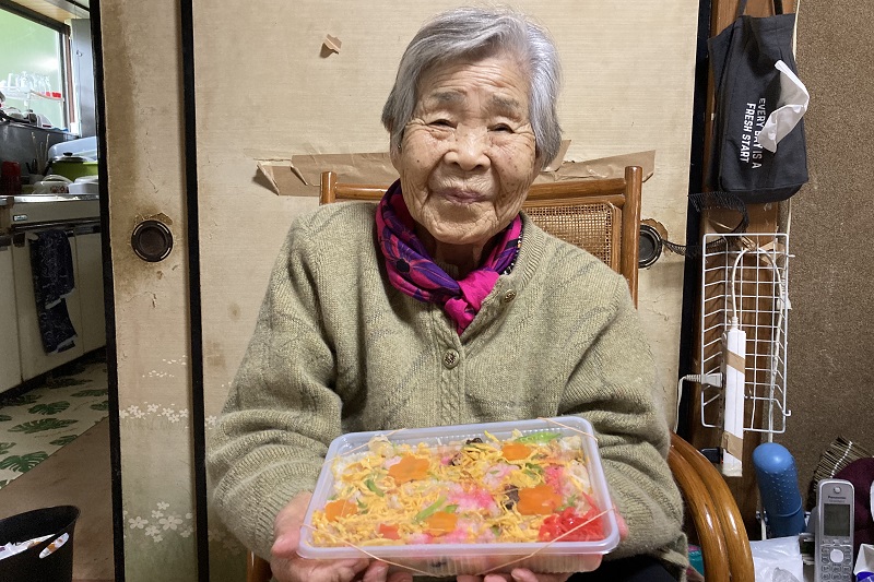 『伊勢屋旅館』の五目御飯を持って笑顔の母ちゃん