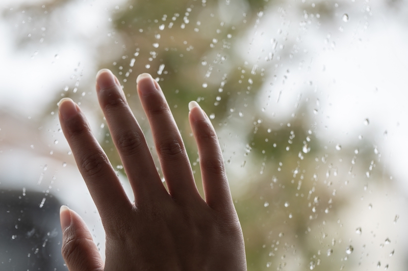 雨が当たる窓に手を当てている