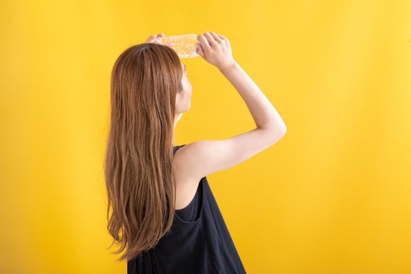 ペットボトルをおでこに当てている女性