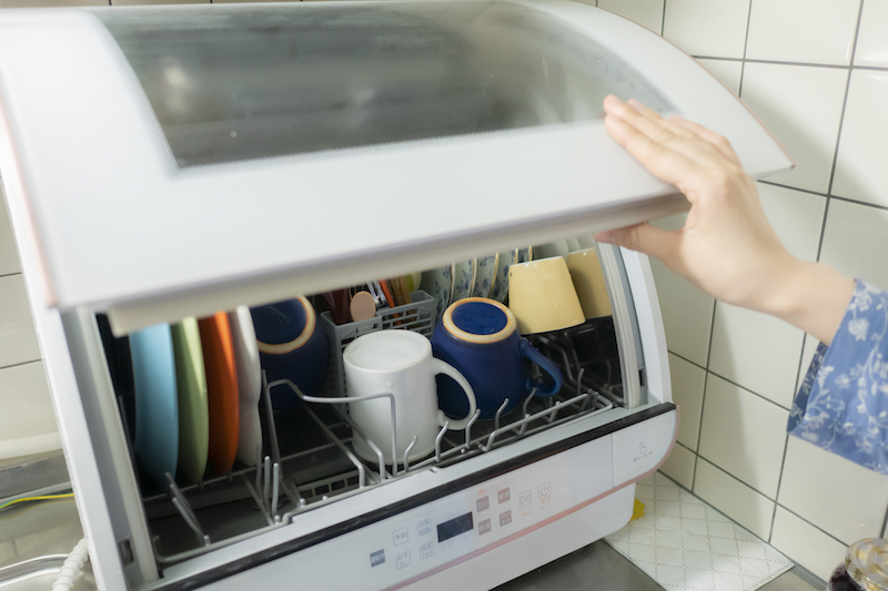 食器がいっぱい入った食洗機の扉を開けている手元