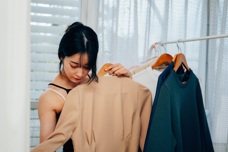 ラックにかかった洋服を当てて選んでいる女性