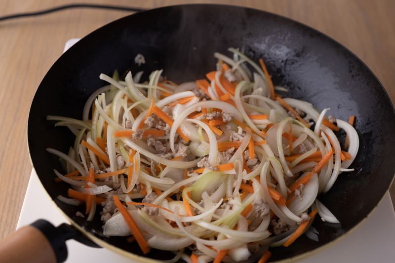 フライパンでごま油を中火で熱し、豚こま肉を炒める。色が変わったらにんじん、玉ねぎを加えてしんなりするまで炒める