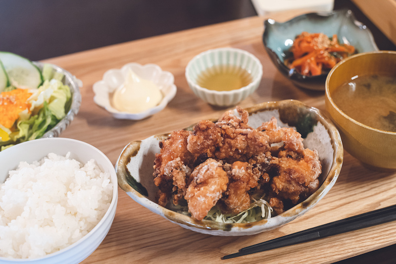 お盆に唐揚げ、ごはん、煮物、サラダ、汁物がのっている