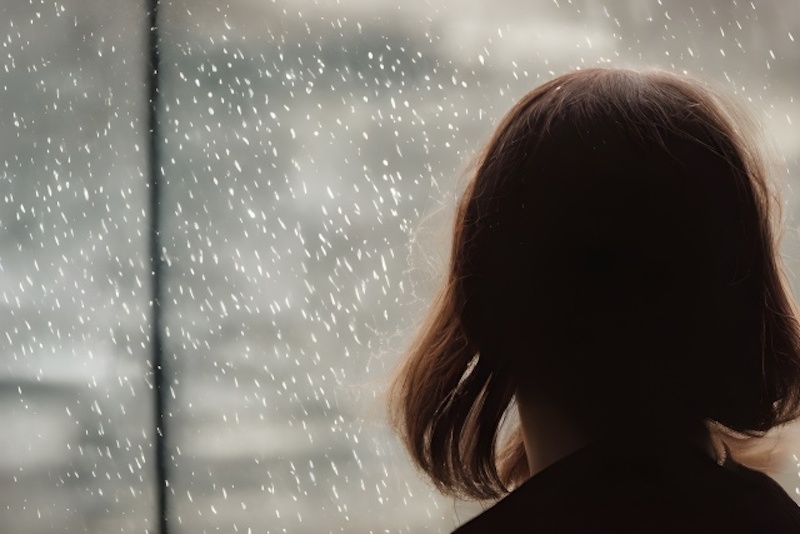 雨の窓の外を眺める女性