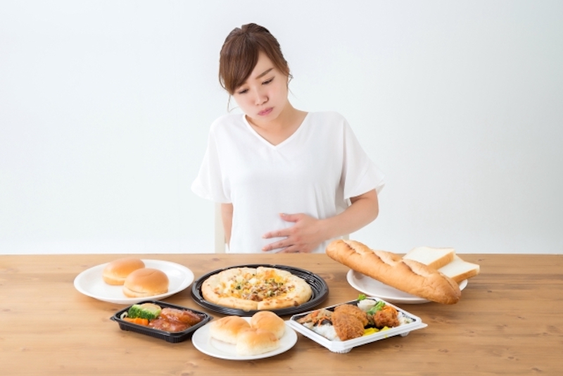 食べ物を前に、お腹を押さえる女性