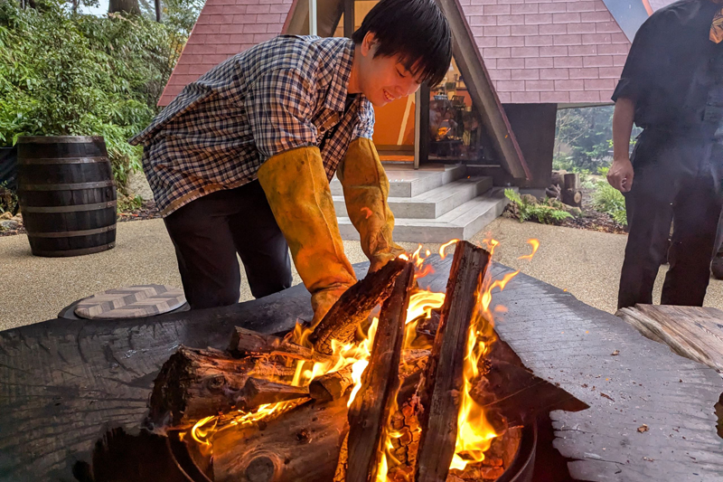 手袋をはめ、焚火の中から焼き芋を収穫中（※季節により体験は変わる）