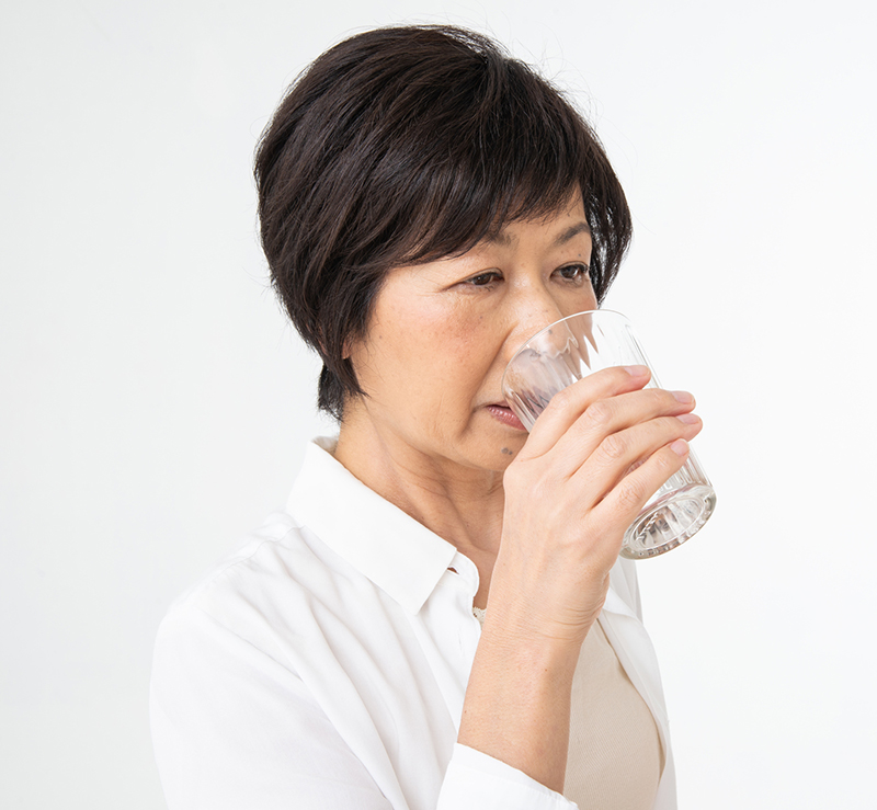 白いシャツを着たショートカットの女性がコップの水を飲んでいる