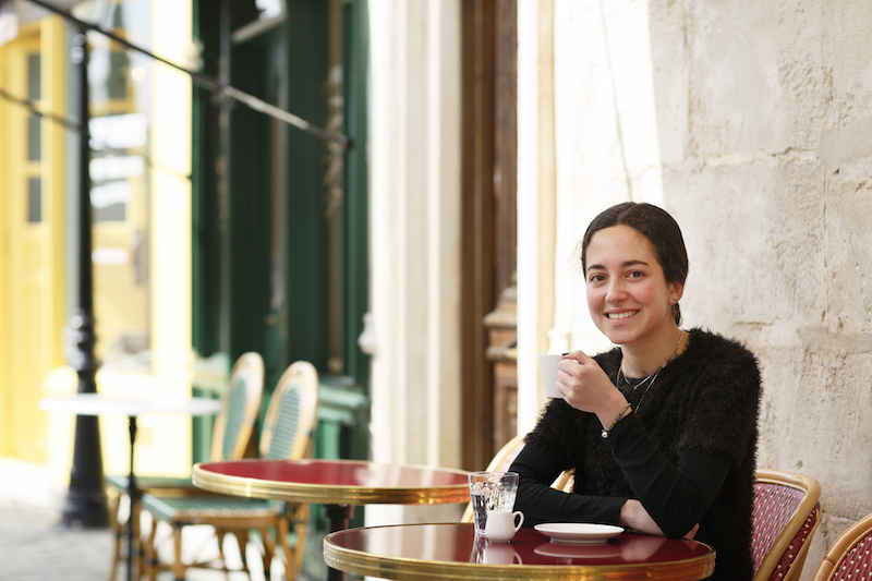 カフェの外の席でコーヒーを飲みながら笑顔のフランス人女性