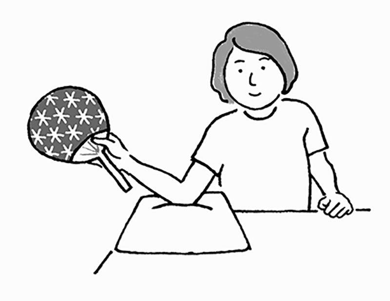 猫背にならないよう姿勢を正して椅子に座る。肩が痛い方の手でうちわを持ち（持ち方は「肩こりのセルフリハビリ」を参照）、机に置いたタオルやクッションの上にひじを置く