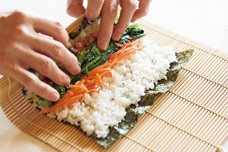 中指と薬指で具材（菜の花）を押さえて巻き始める