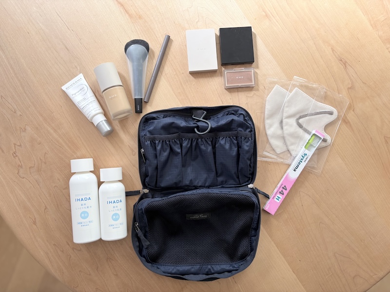 左下から時計回りに、化粧水と乳液、日やけ止め、リキッドファンデーション、チークブラシ、アイライナー、アイシャドウ、アイブロウ、チーク、マスク2枚、歯ブラシ（シャンプーやボディソープは備え付けのものを活用する想定）